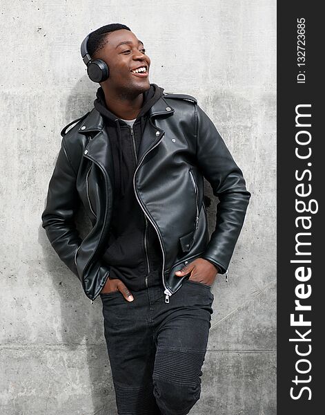 Smiling black man in leather jacket listening to music with headphones