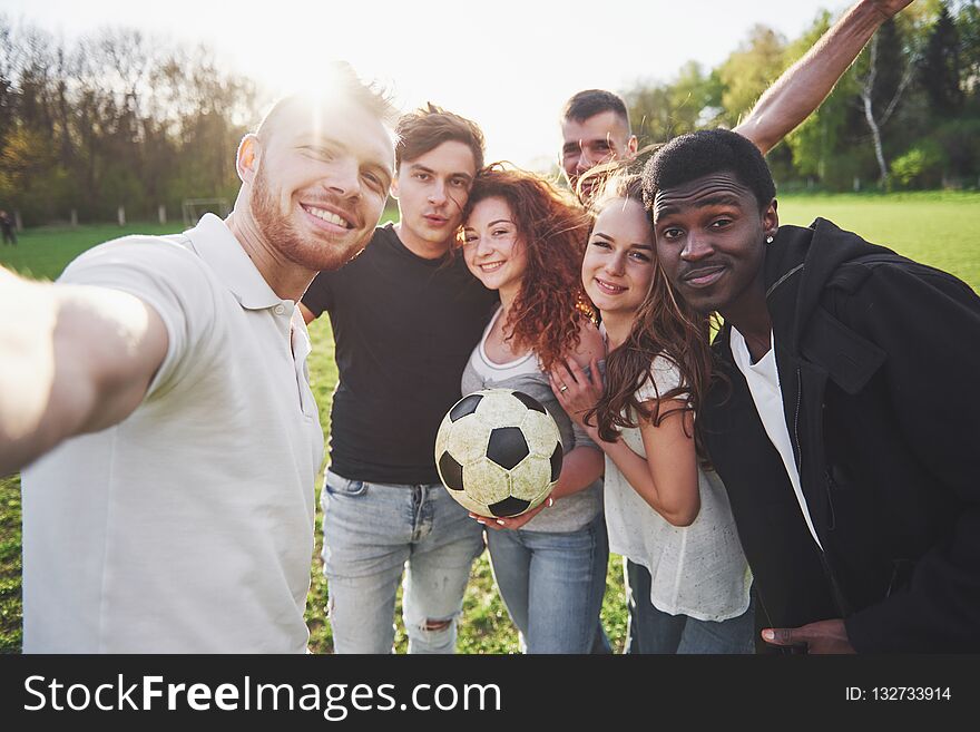 A group of friends in casual outfit do sephi on the soccer field. People have fun and have fun. Active rest and scenic sunset.