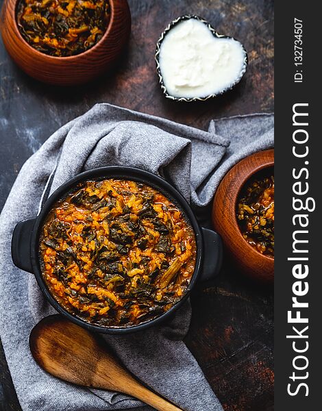 Spinach stew with rice in black pot on dark background