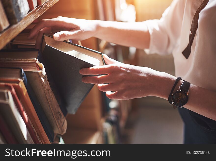 A young girl student looking for literature near the bookshelves in the old library,