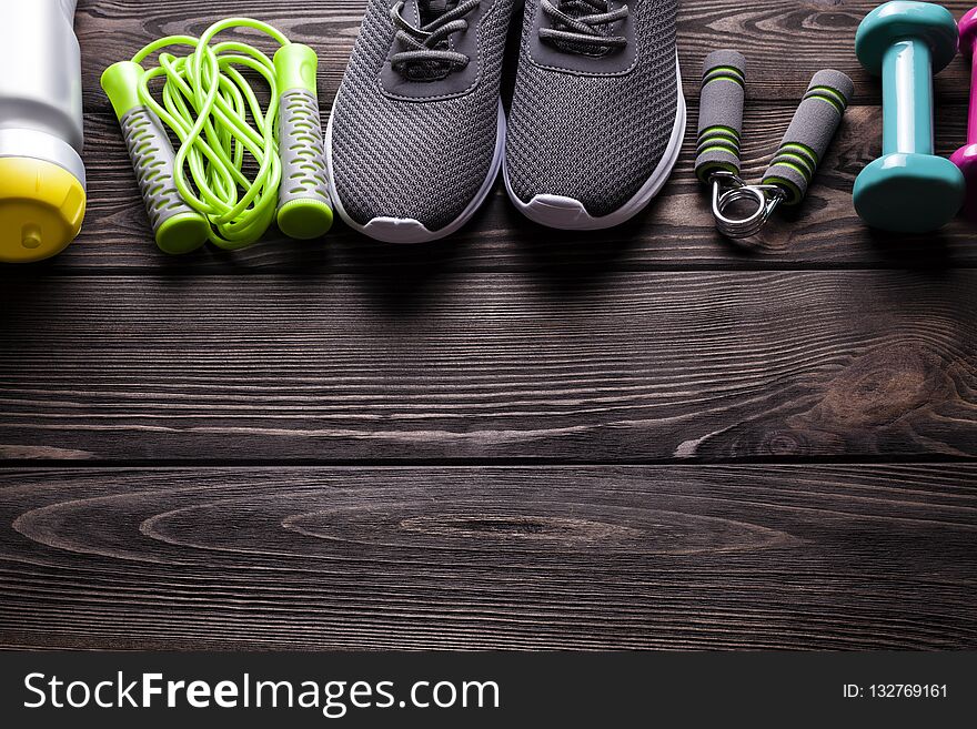 Fitness equipment - water, jumping rope, sneakers and dumbbell on wooden board