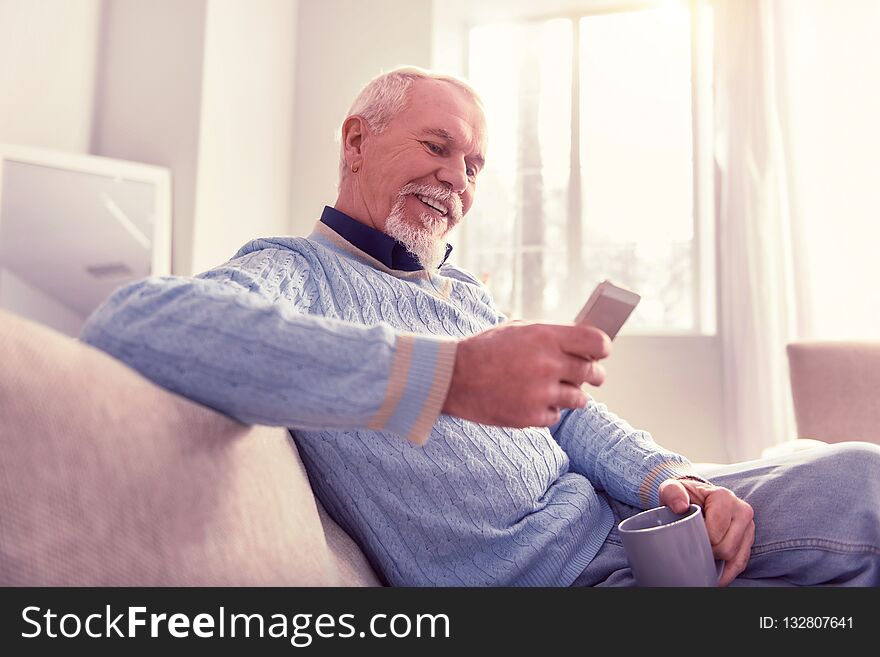 Radiant senior checking. Radiant senior checking content on his mobile phone while relaxing at home. Radiant senior checking. Radiant senior checking content on his mobile phone while relaxing at home