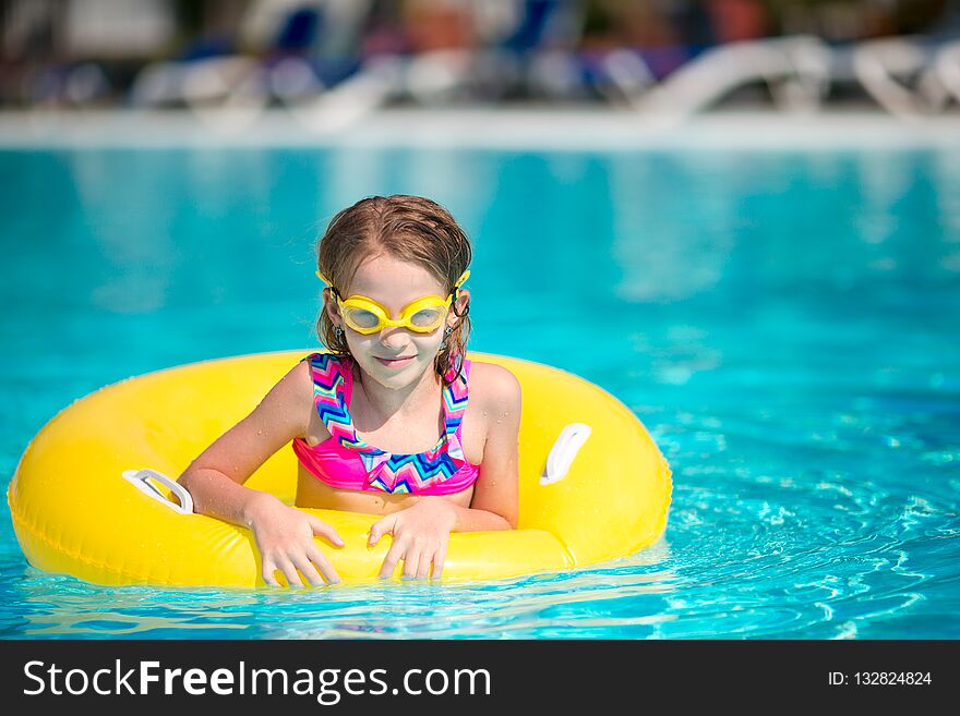 Little girl with inflatable rubber circle having fun in swimming pool
