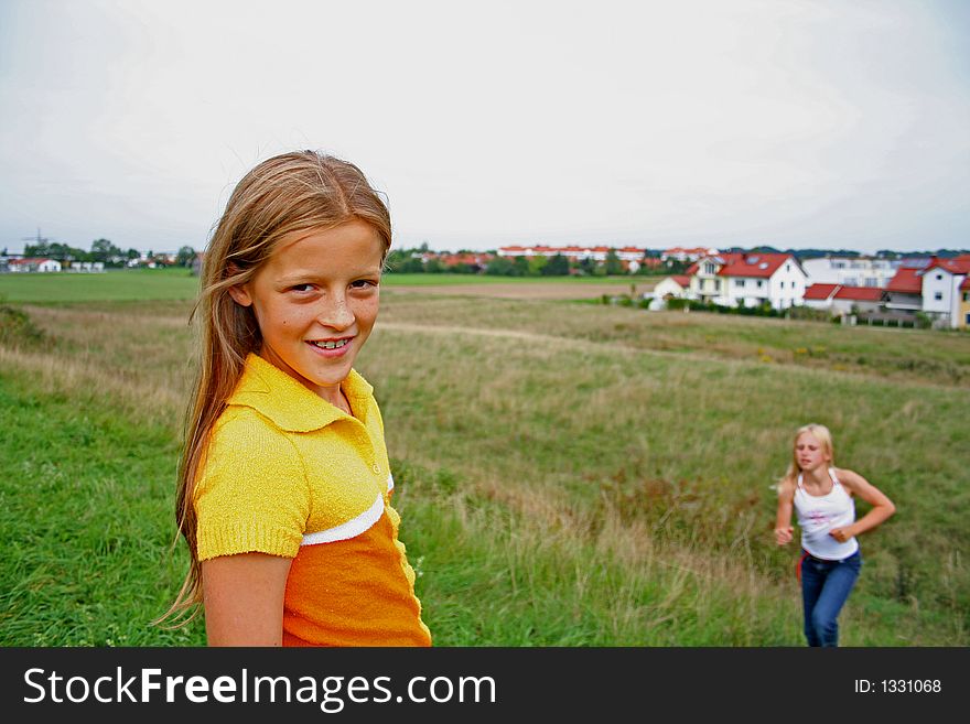 Two girls, one posing other climbing hill behind. Two girls, one posing other climbing hill behind