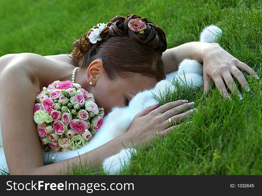 The beautiful bride with a wedding bouquet lays on a grass