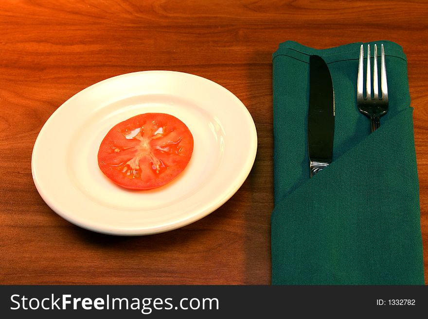 Single tomato slice with fork and knife