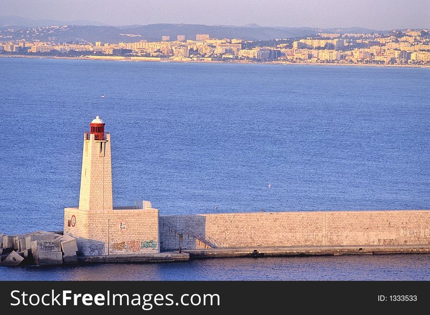 Beacon and jetty at sunrise in the entrance of Nice port in french riviera, europe, part of the city in the background. Beacon and jetty at sunrise in the entrance of Nice port in french riviera, europe, part of the city in the background