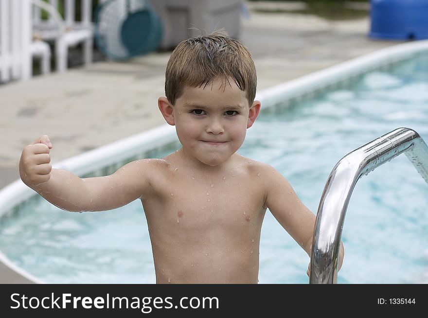 Young boy flexing muscle poolside. Young boy flexing muscle poolside