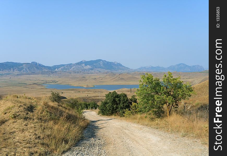 Road and lake in valley, far mountains