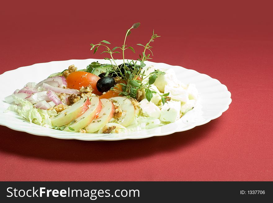 Healthy feta-cheese salad with fresh cucumber tomato apple and onion slices and olives over royal red background