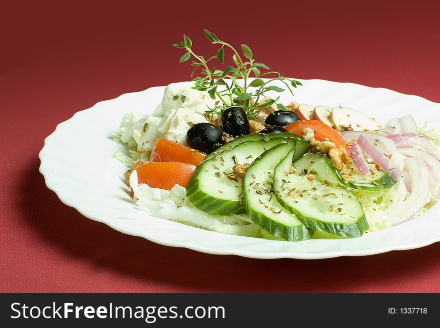 Healthy feta-cheese salad with fresh cucumber, tomatoes, apple and onion slices and olives over royal red background