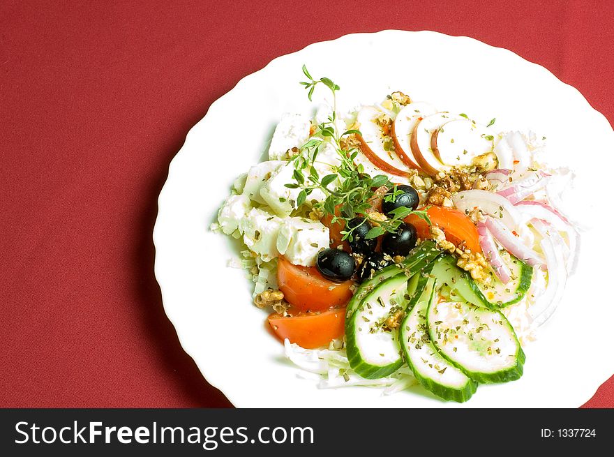 Healthy feta-cheese salad with fresh cucumber tomato apple and onion slices and olives over royal red background