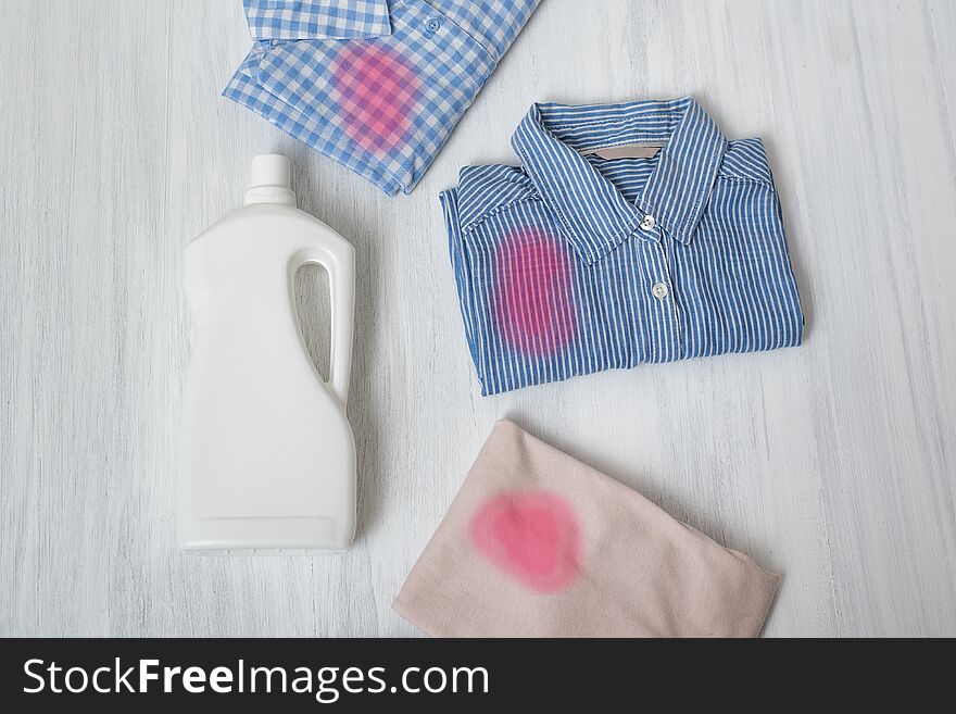 Clothes with stains and a bottle of detergent. Top view