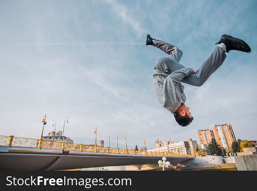 Sportive man doing acrobatic exercise while jumping with city behind. Sportive man doing acrobatic exercise while jumping with city behind