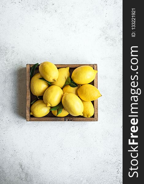 Lemons with green leaves in box on white stone background, top view, copy space. Organic fresh citrus fruits lemons