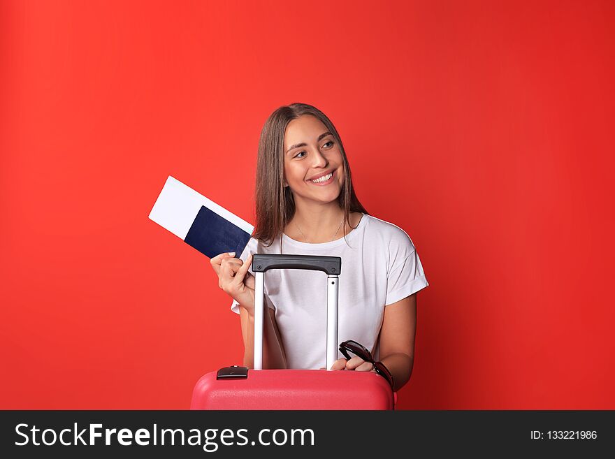 Young tourist girl in summer casual clothes, with sunglasses, red suitcase, passport isolated on red background.