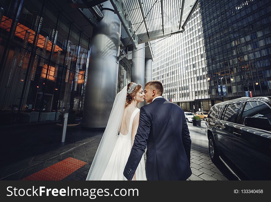 Elegant bride in a white dress and veil. Handsome groom in a blue suit. Couple in a big town. Elegant bride in a white dress and veil. Handsome groom in a blue suit. Couple in a big town