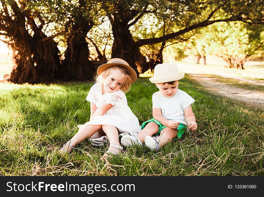 Two children in hats sitting in green grass. Beautiful spring park.