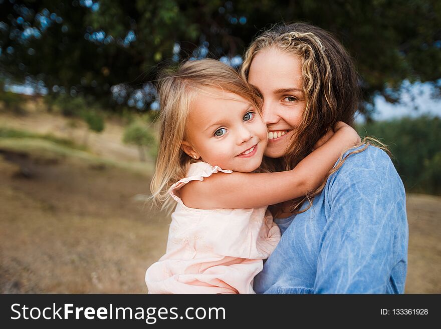 Curly blond mother with daughter walking in the field hugging and laughing. Curly blond mother with daughter walking in the field hugging and laughing.
