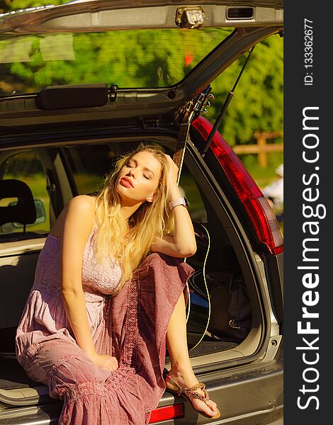 Travel vacation hitchhiking concept. Summer girl hippie style sitting on hatchback car with acoustic guitar enjoying sunlight. Travel vacation hitchhiking concept. Summer girl hippie style sitting on hatchback car with acoustic guitar enjoying sunlight