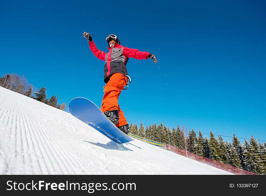 Snowboarder in the air while riding on the slope in the mountains on a beautiful sunny winter day. Blue sky on the background active lifestyle sports concept