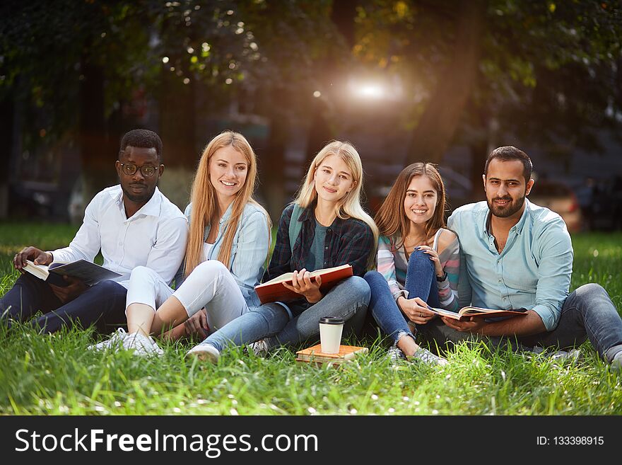 Mixed-race group of students sitting together on green lawn of university campus
