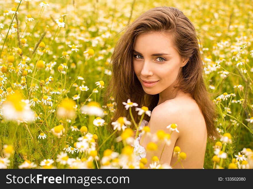 Photo of pretty brunette woman in chamomile field, cute female enjoying smell of daisy, sweet girl with closed eyes relaxed on flowers meadow, spring nature, having fun outdoor