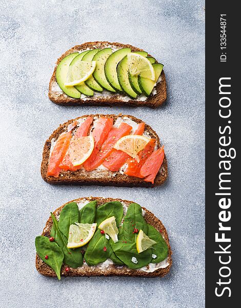 Open sandwiches with spinach and avocado salmon on a grey table.
