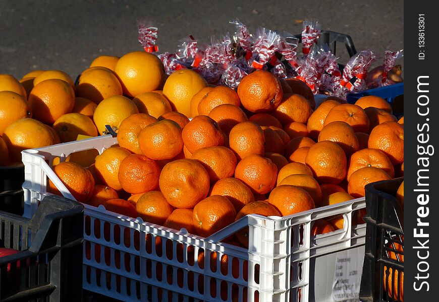 Outdoor fruit market detail with bright orange mandarins and red and white Christmas-styled wrapped other decorative items in white plastic container box in open space with gray background