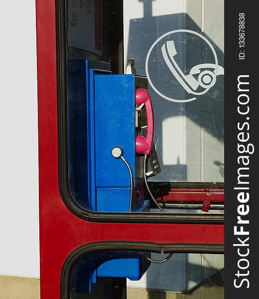 Retro style blue and pink land line public telephone in red phone booth in daylight with shadow and phone symbol on glass. Retro style blue and pink land line public telephone in red phone booth in daylight with shadow and phone symbol on glass