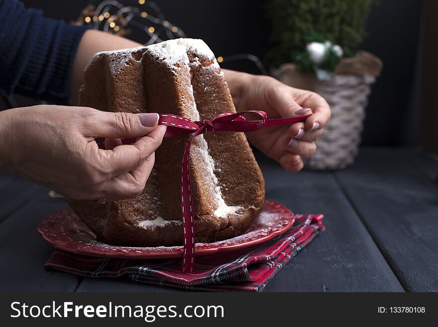 Italian Christmas cupcake with powdered sugar. Traditional festive pastries in female hands. Dark background and decor with lights. Dark photo. Free space for tex