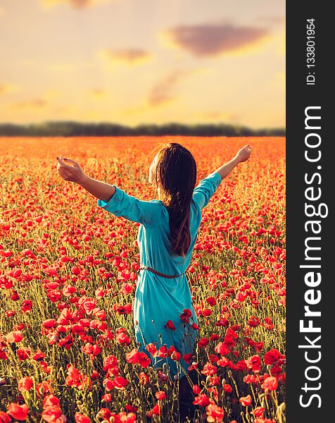 Happy young woman standing with raised arms in red poppies meadow at sunset. Happy young woman standing with raised arms in red poppies meadow at sunset.