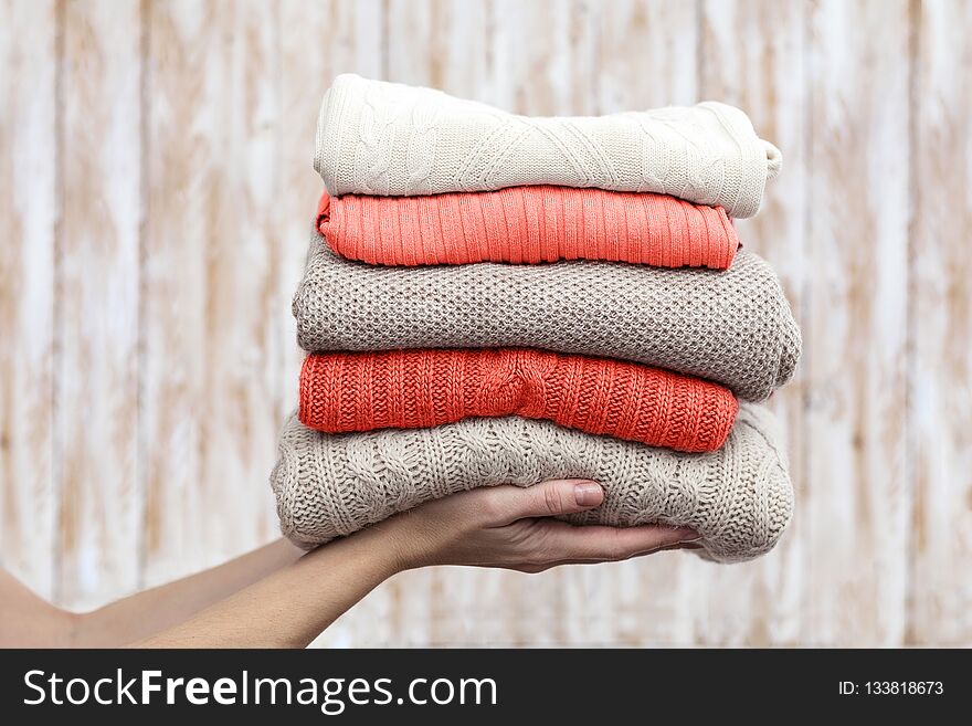 Stack of warm pastel sweaters, holding in hands. Living Coral creative and moody color of the picture