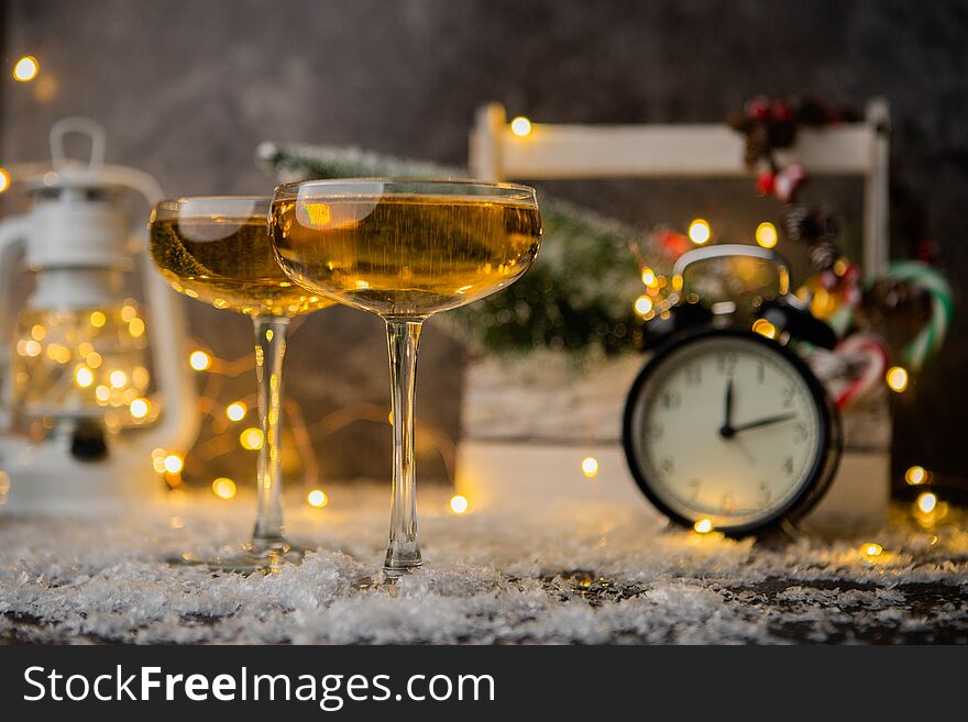 Picture of two wine glasses on table with snow on blurred background with Christmas tree, lantern, clock. Picture of two wine glasses on table with snow on blurred background with Christmas tree, lantern, clock