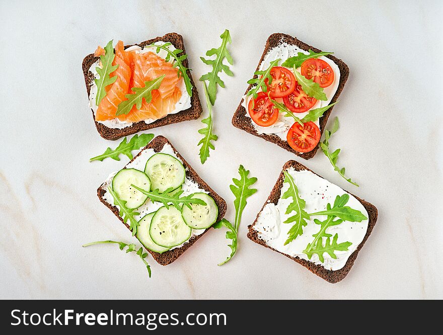 Smorrebrod - traditional Danish sandwiches. Black rye bread with salmon, cream cheese, cucumber, tomatoes on wooden background