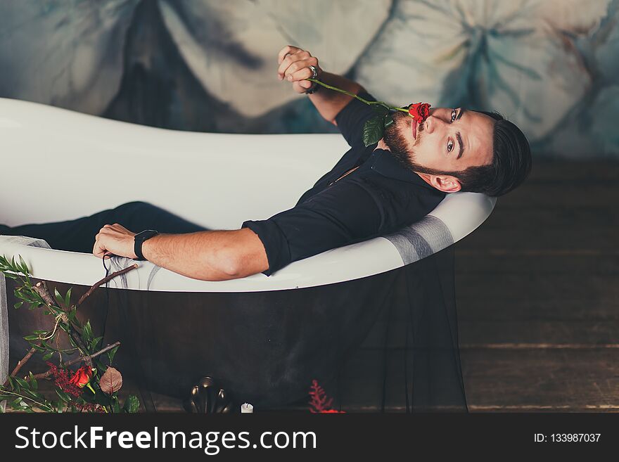 Brutal stylish man with scarlet Rose sits in bath. Brutal stylish man with scarlet Rose sits in bath