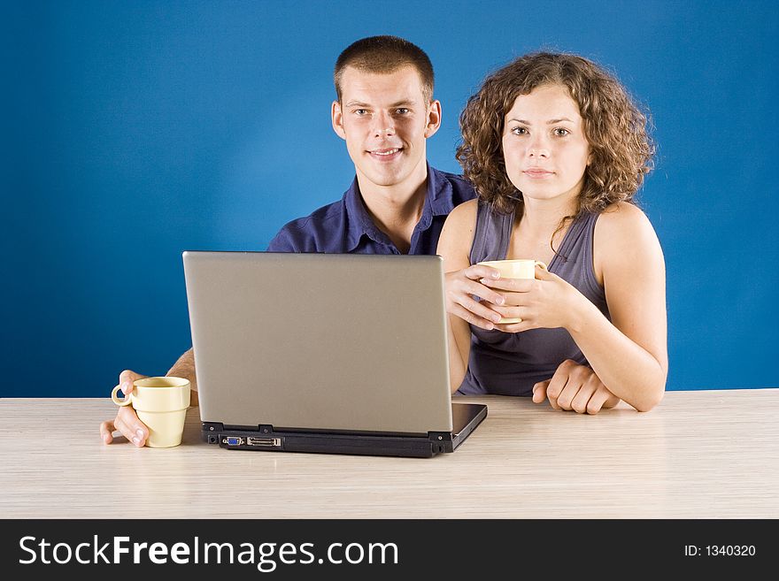 Young couple at the table with laptop + blue background