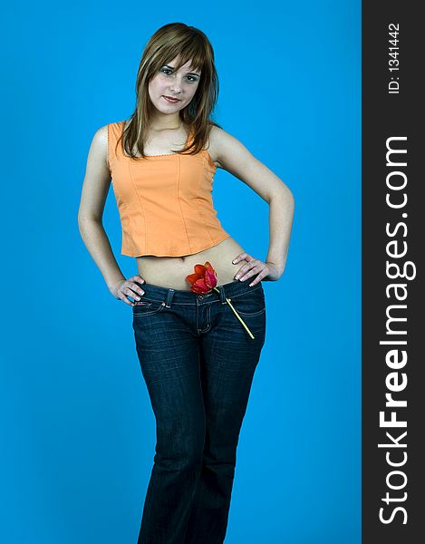 Beautiful young girl smiling and having a red tulip at her waist, like a pistol; isolated on blue background. Beautiful young girl smiling and having a red tulip at her waist, like a pistol; isolated on blue background