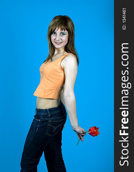 Young girl with nice looks and make-up, smiling and looking happy; holding a red tulip at her back; isolated on blue. Young girl with nice looks and make-up, smiling and looking happy; holding a red tulip at her back; isolated on blue