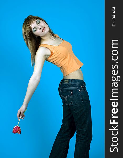 Beautiful young girl posing in a studio, holding a red tulip in her hand and stretching over her back with eyes closed, isolated on blue background. Beautiful young girl posing in a studio, holding a red tulip in her hand and stretching over her back with eyes closed, isolated on blue background