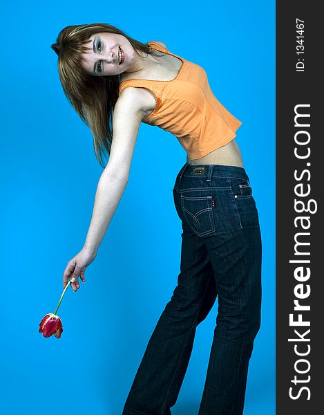 Beautiful young girl posing in a studio, holding a red tulip in her hand and stretching over her back, smiling, isolated on blue background. Beautiful young girl posing in a studio, holding a red tulip in her hand and stretching over her back, smiling, isolated on blue background