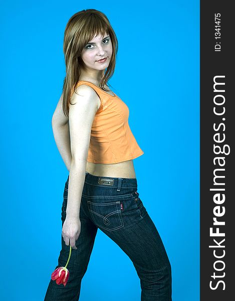 Young girl with nice looks and make-up; holding a red tulip at her back; posing in a studio; isolated on blue. Young girl with nice looks and make-up; holding a red tulip at her back; posing in a studio; isolated on blue