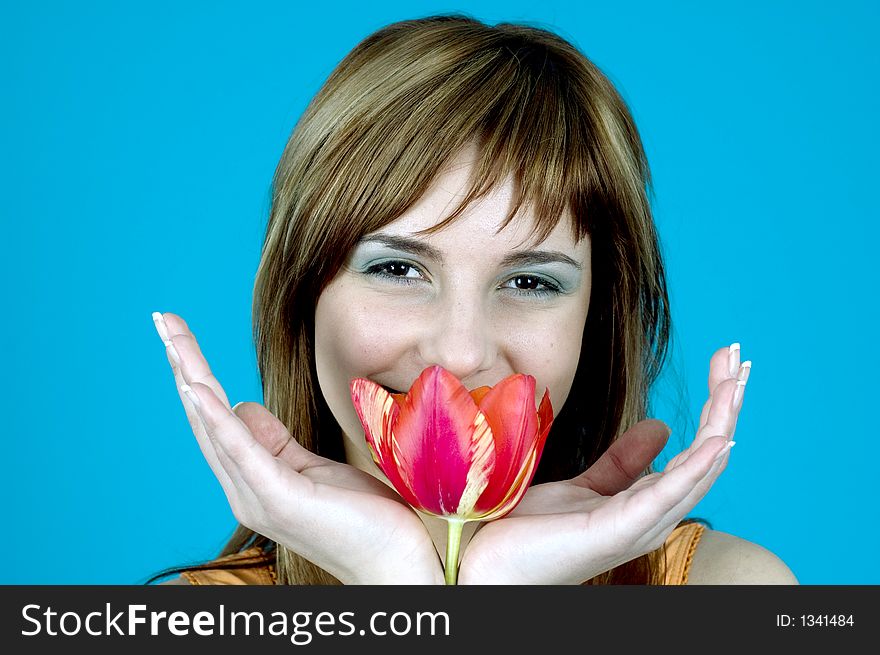 Portrait of a beautiful young girl smiling and holding a tulip between her hands, nice make-up; isolated on blue background. Portrait of a beautiful young girl smiling and holding a tulip between her hands, nice make-up; isolated on blue background
