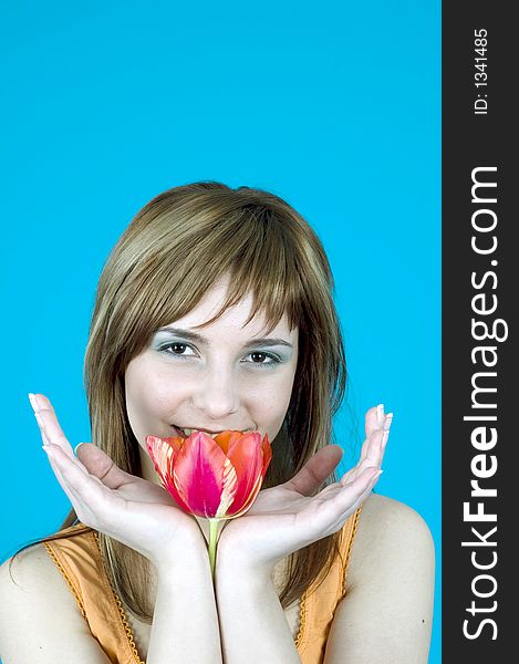 Portrait of a beautiful young girl smiling and holding a tulip between her hands, nice  make-up; isolated on blue background. Portrait of a beautiful young girl smiling and holding a tulip between her hands, nice  make-up; isolated on blue background