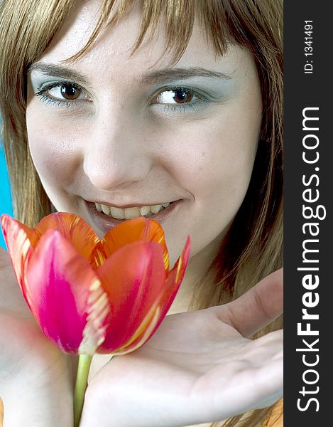 Portrait of a beautiful young girl smiling and holding a tulip between her hands, nice  make-up; isolated on blue background. Portrait of a beautiful young girl smiling and holding a tulip between her hands, nice  make-up; isolated on blue background