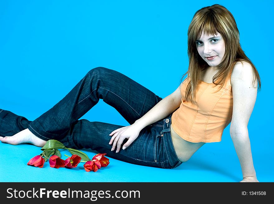Portrait of a beautiful young girl laying on the floor next to a bouquet of tulips; nice smile; teenager looks and attitude; isolated on blue background. Portrait of a beautiful young girl laying on the floor next to a bouquet of tulips; nice smile; teenager looks and attitude; isolated on blue background