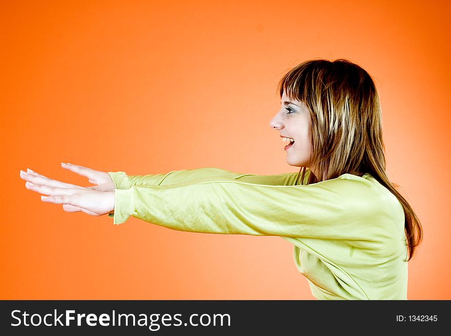 Young and good-looking girl smiling and holding her hands in front of her face, looking like she's doing exercises; isolated on orange background. Young and good-looking girl smiling and holding her hands in front of her face, looking like she's doing exercises; isolated on orange background