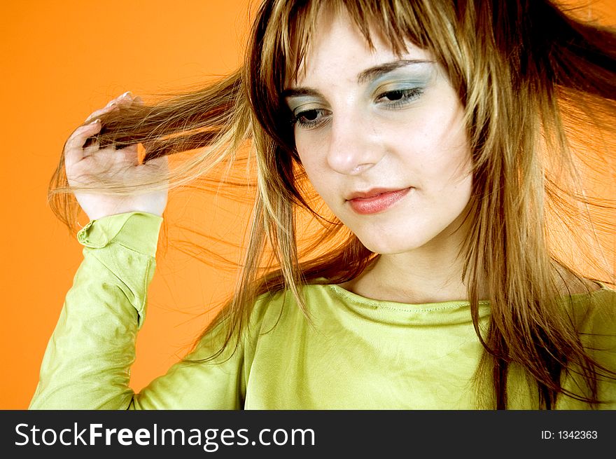 Beautiful young girl posing in a studio, pulling her hair with both hands, looking like she's thinking about the next haircut or colour; isolated on orange. Beautiful young girl posing in a studio, pulling her hair with both hands, looking like she's thinking about the next haircut or colour; isolated on orange