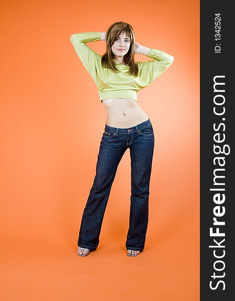 Beautiful young girl standing and holding her hands behind her head, looking relaxed and confident; isolated on orange. Beautiful young girl standing and holding her hands behind her head, looking relaxed and confident; isolated on orange