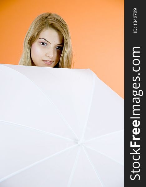 Portrait of a beautiful blond girl looking shy behind an umbrella; orange background. Portrait of a beautiful blond girl looking shy behind an umbrella; orange background